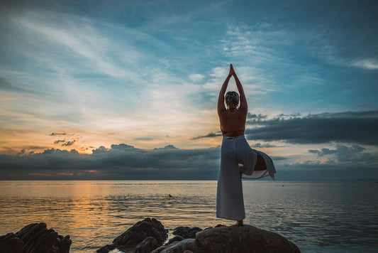 Femme en posture de yoga au bord de l’eau au coucher du soleil – récupération post-effort, relaxation et équilibre après le sport